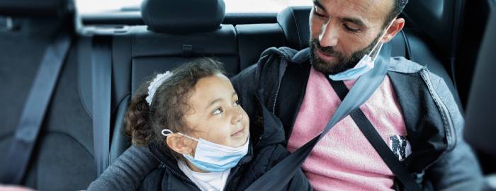 A father and daughter in the back of a car looking at one another.