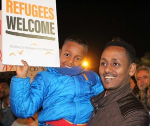 A father and son holding a sign that says "Refugees welcome"