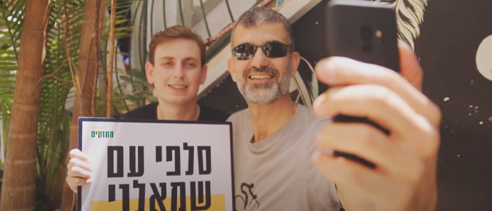 Advocates from Mehazkim take a selfie while holding up a protest sign.